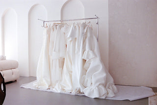 White wedding dresses hanging on a rack in a bright room with white walls.