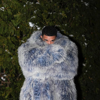 Person wearing a large blue fur coat standing in a snowy forest at night.
