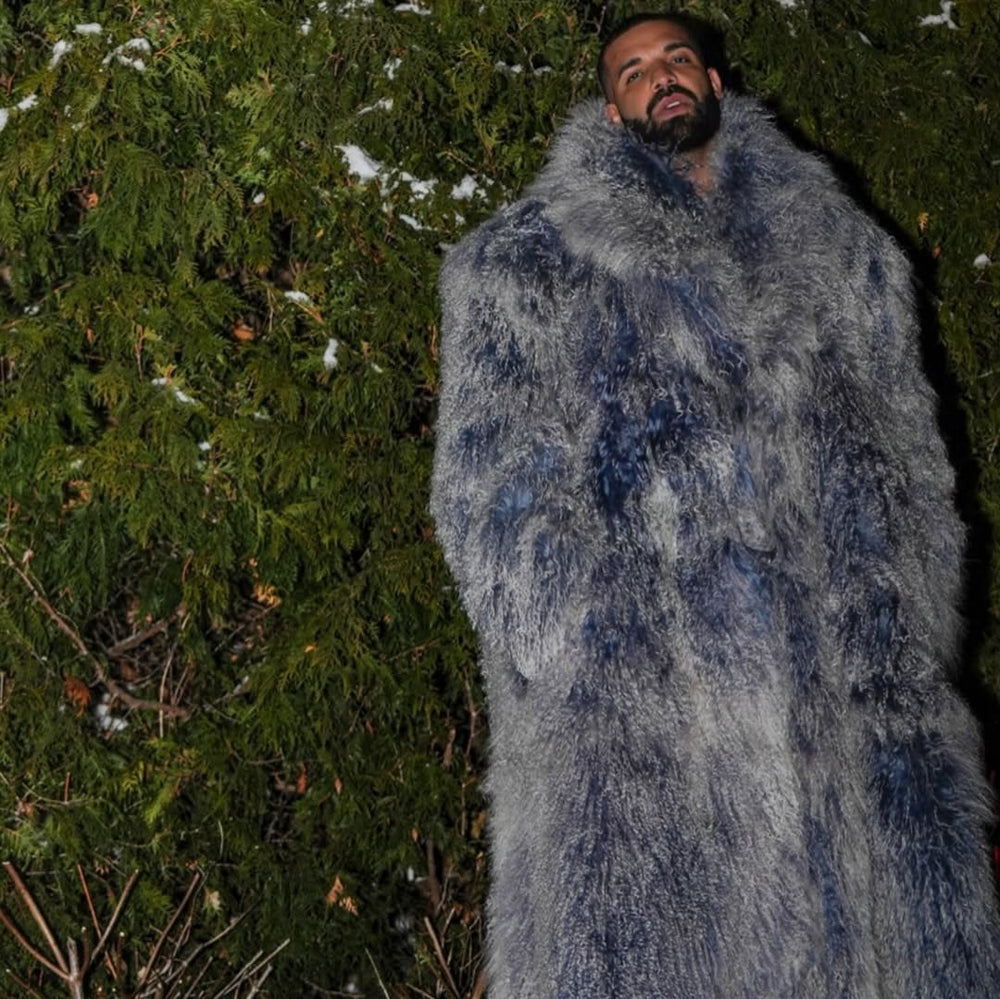 Person wearing a long, fluffy coat standing against a green, leafy background