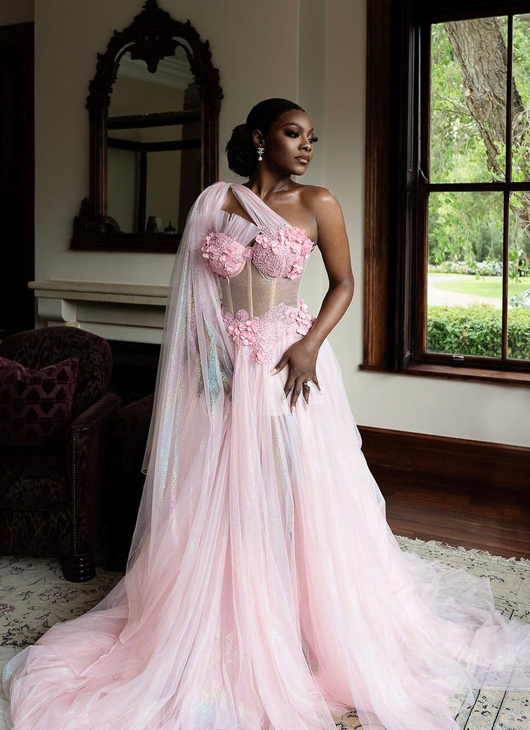 Dihma in a ZM pink floral one-shoulder prep bridal robe standing in a room in capetown with a window, chair and mirror.