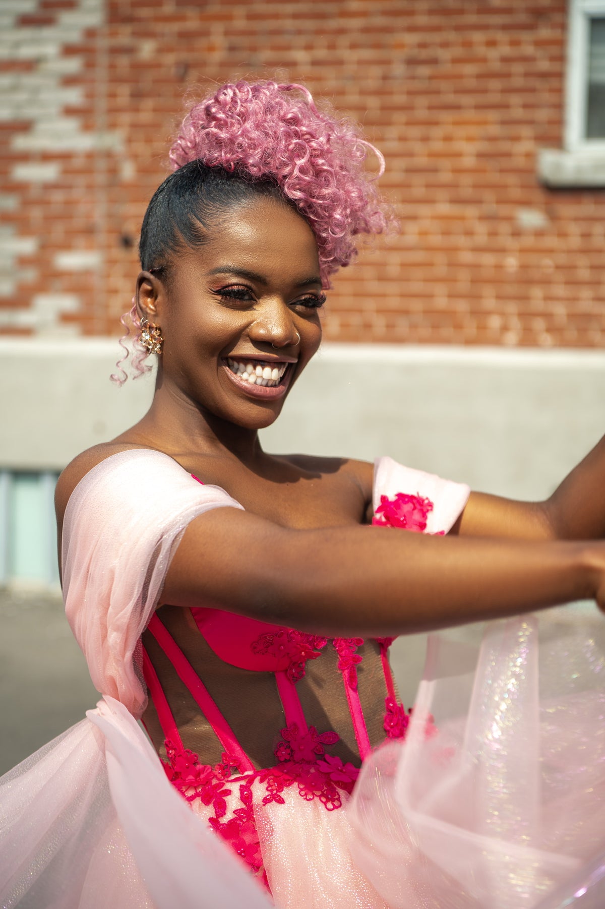 Chizoba Martin smiling in a hot pink Zoba Martin special occasion birthday dress with floral appliqué and blush tulle.